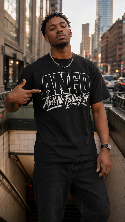 A man wearing a black graphic t-shirt with 'ANFO Aint No Falling Off' printed in white, standing in an urban subway entrance.