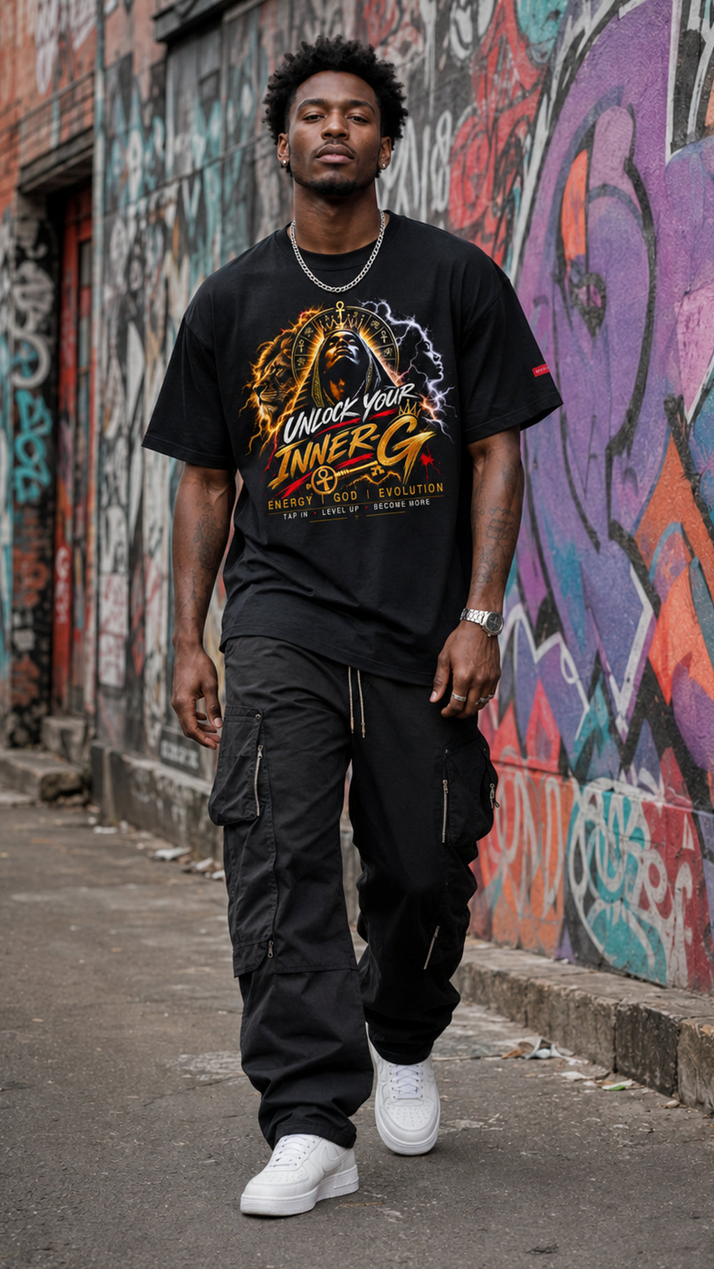 Man wearing the black Unlock Your Inner-G Graphic Tee with a yellow-and-orange design, walking along an urban street with colorful graffiti walls.