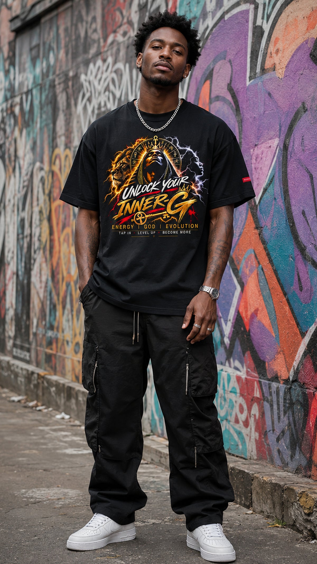 Man wearing the black Unlock Your Inner-G Graphic Tee with a yellow, orange and white design, standing in front of a colorful graffiti wall.
