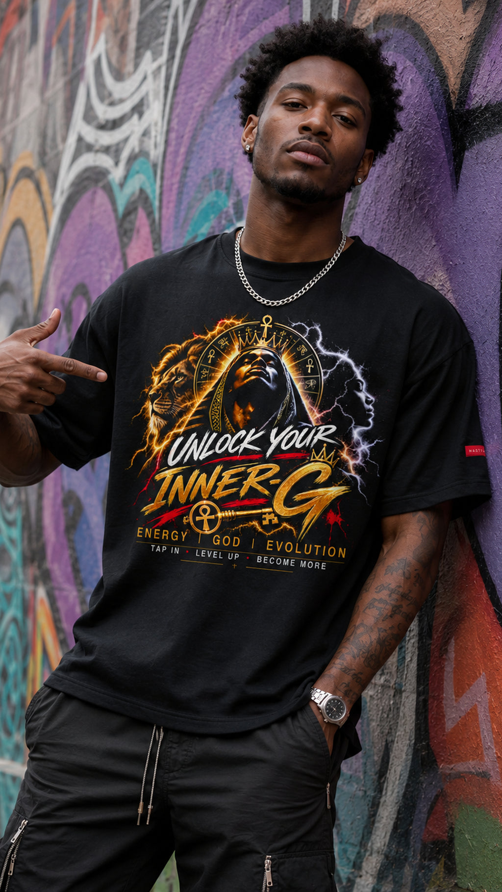 Man wearing the black Unlock Your Inner-G Graphic Tee with a fiery yellow-and-orange design, standing in front of a colorful graffiti wall.