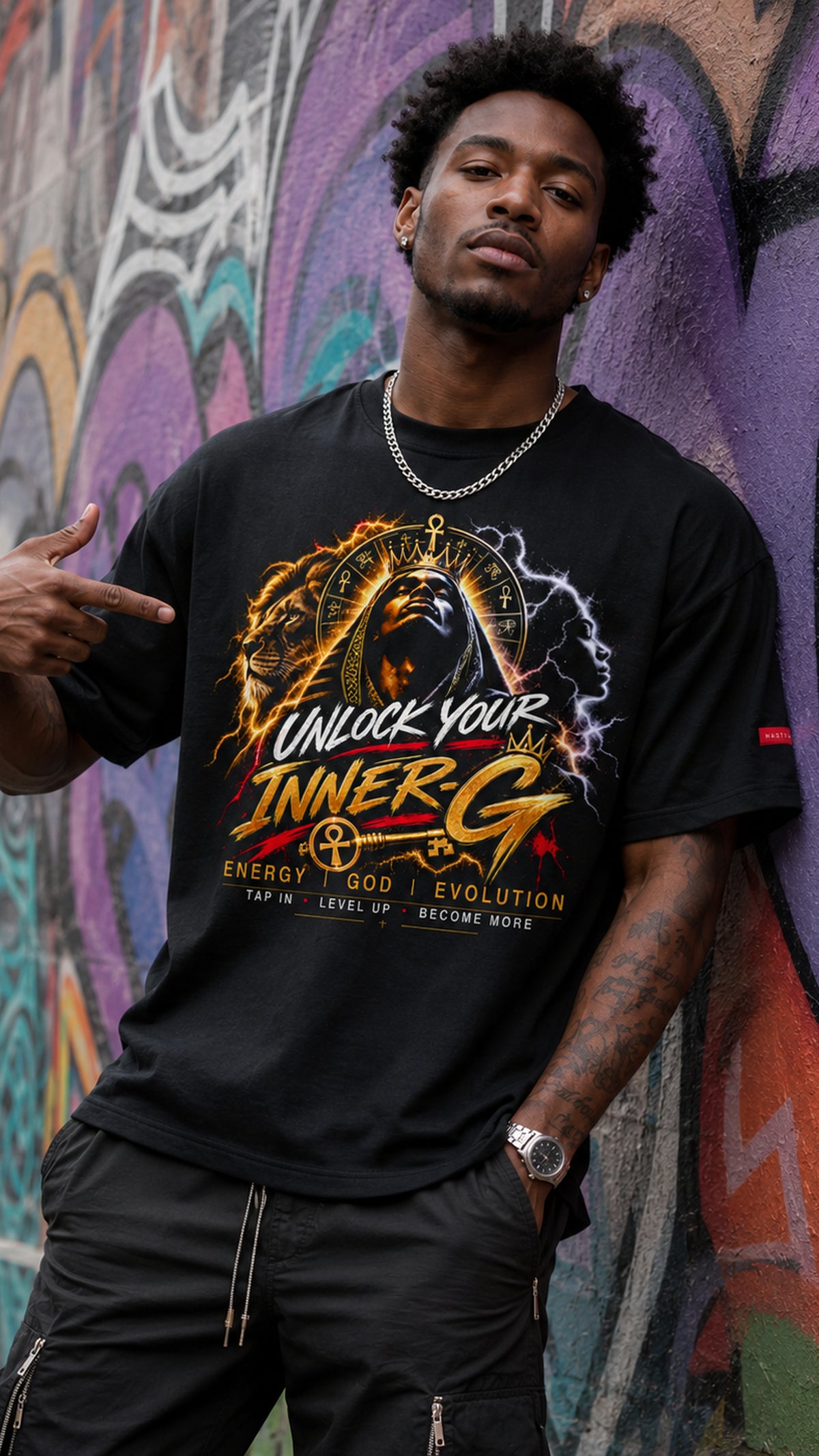 Man wearing the black Unlock Your Inner-G Graphic Tee with a fiery yellow-and-orange design, standing in front of a colorful graffiti wall.